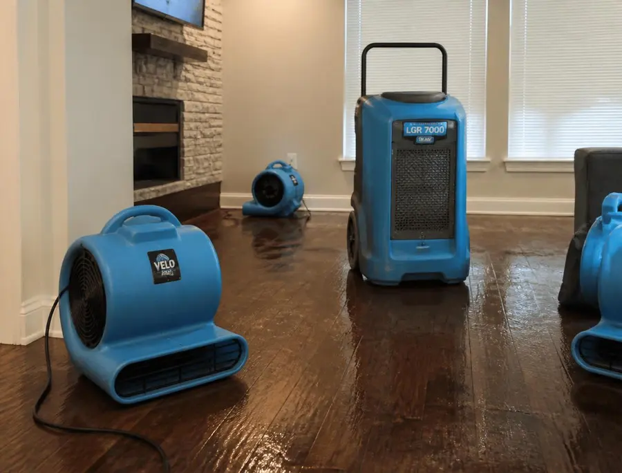 Air movers and a dehumidifier drying a damp hardwood living room floor